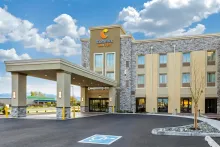 Exterior view of a modern Comfort Suites hotel with a covered entrance and a handicap parking space in the foreground.